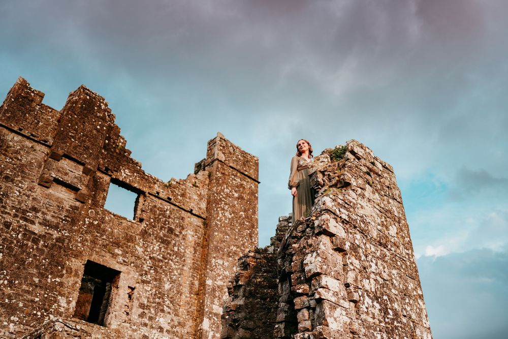 Woman standing atop ancient stone castle ruins against a dramatic cloudy sky in Ireland.
