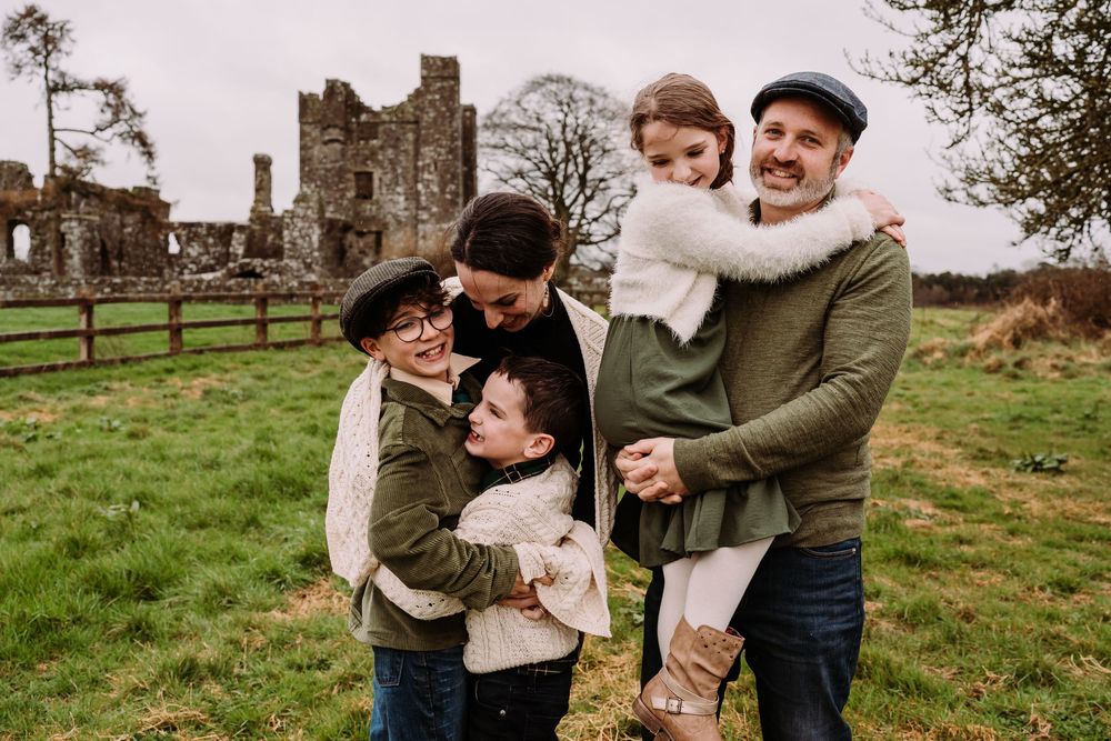 Happy family of five laughing together outdoors near ancient ruins on a green Irish countryside.