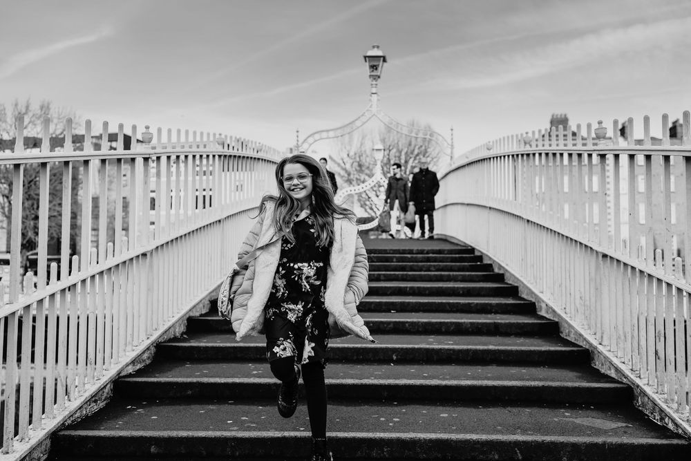 Black and white photo of a smiling woman walking down steps on Ha'penny Bridge in Dublin, Ireland.