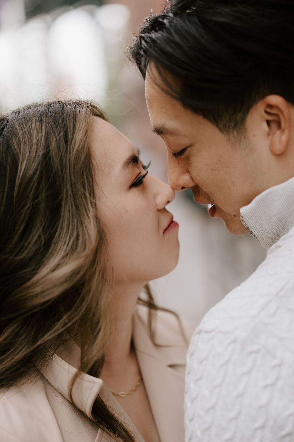 A couple shares a romantic almost-kiss moment, faces close together, in a soft, blurred outdoor setting.
