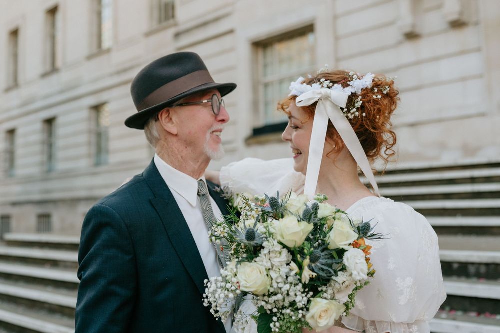Elegant older couple in wedding attire share an intimate moment holding a white floral bouquet.