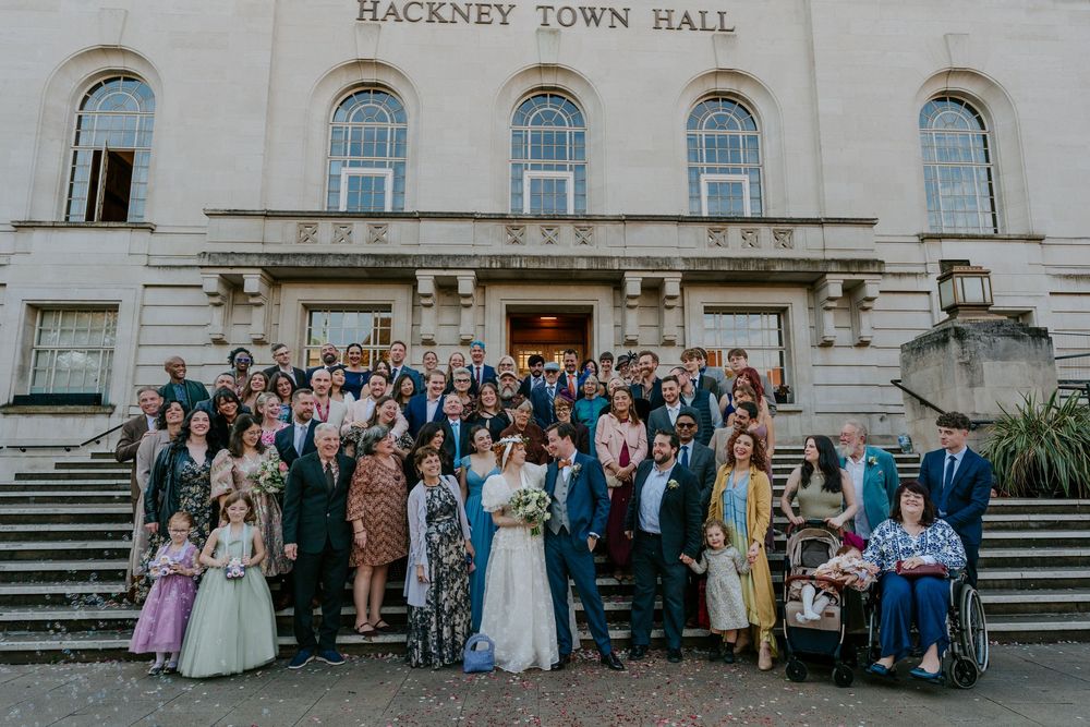 Large wedding group photo on steps outside Hackney Town Hall, bride and groom surrounded by guests.
