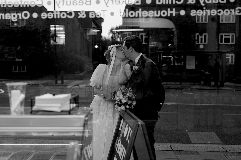 Bride and groom share a kiss reflected in a shop window in black and white urban wedding photo.