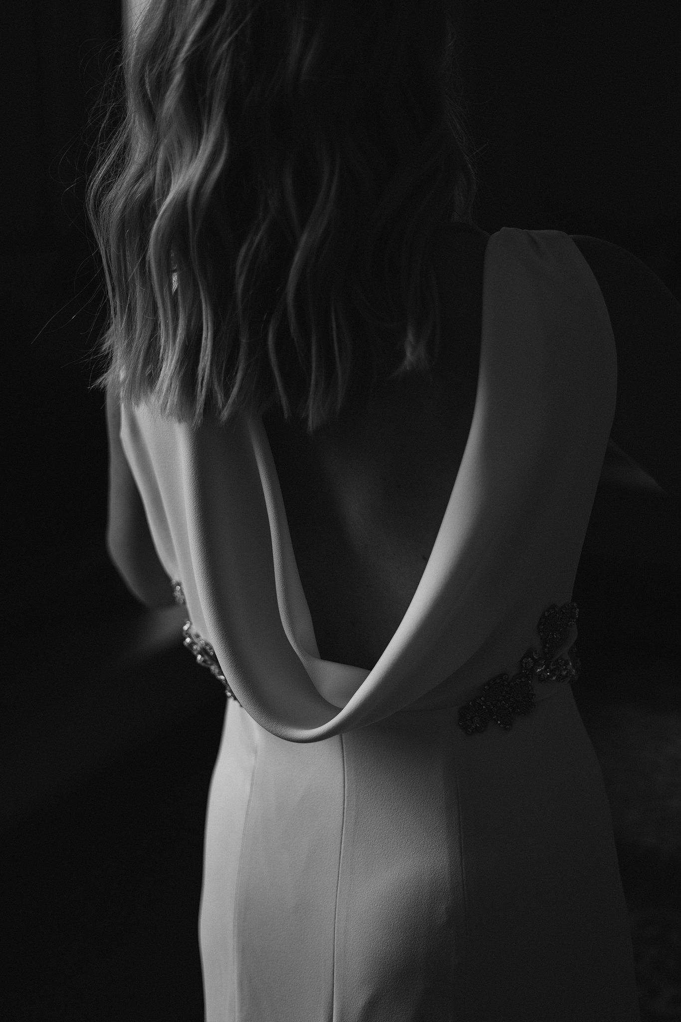 Black and white photo of a woman in an elegant backless white gown with floral embellishments.