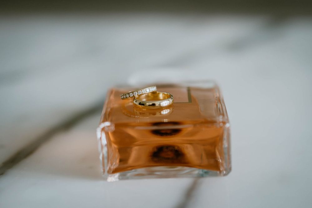 Gold wedding bands resting on a square glass perfume bottle, symbolizing love and commitment.
