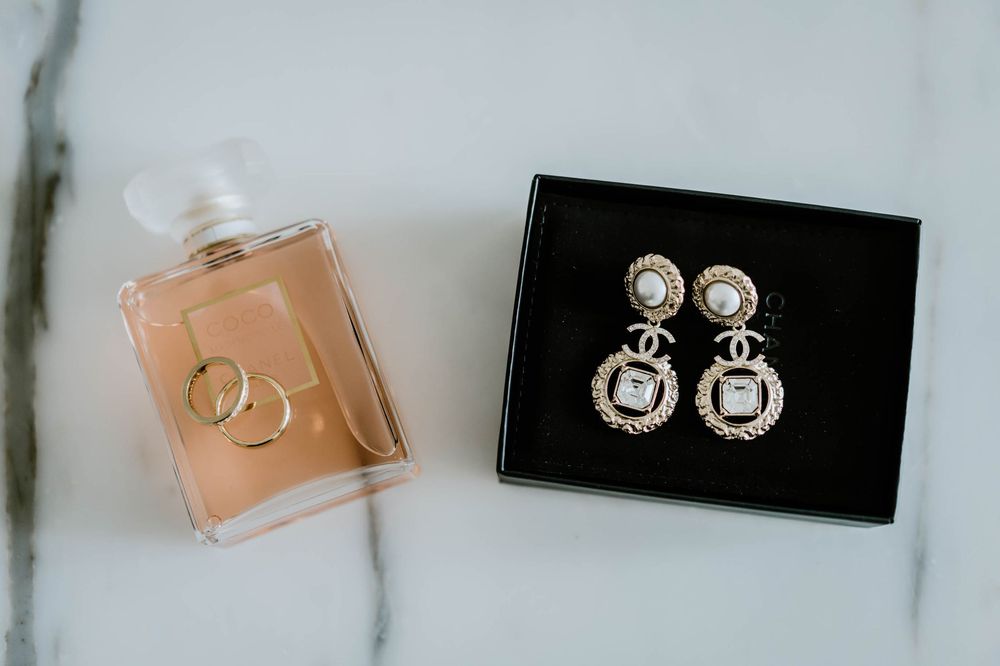 Gold pearl Chanel drop earrings in black box beside Coco Chanel perfume bottle and gold rings on marble.