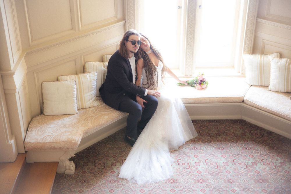 Bride and groom share intimate moment seated together on window bench in elegant vintage interior.