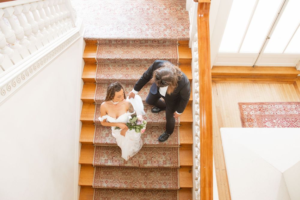 Aerial view of bride and groom descending wooden staircase in bright elegant wedding venue.