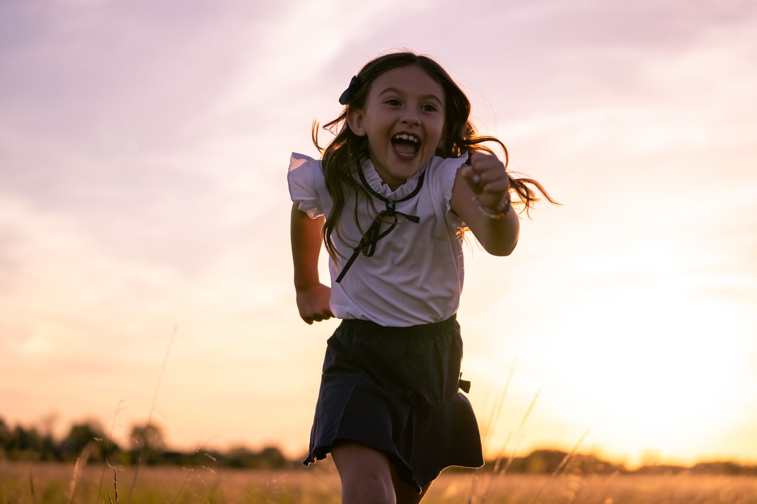 A joyful young girl in a school uniform runs through a golden field at sunset with a big smile.