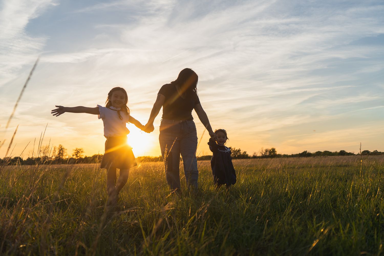 Silhouette of mother and two children playing in a sunlit field at golden sunset hour.