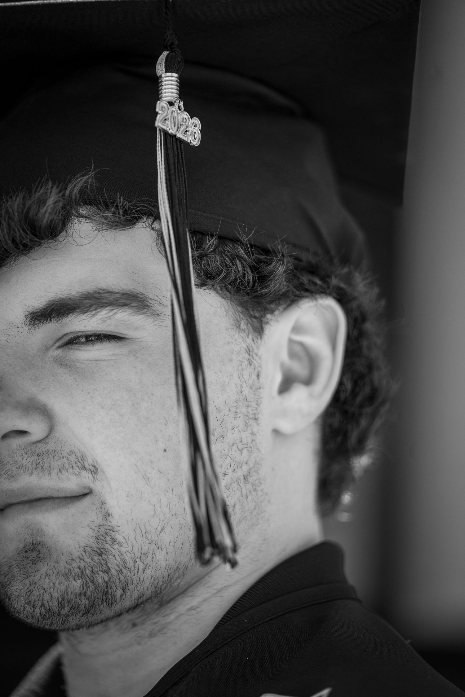 Black and white close-up portrait of a young male graduate wearing a 2023 graduation cap with tassel.