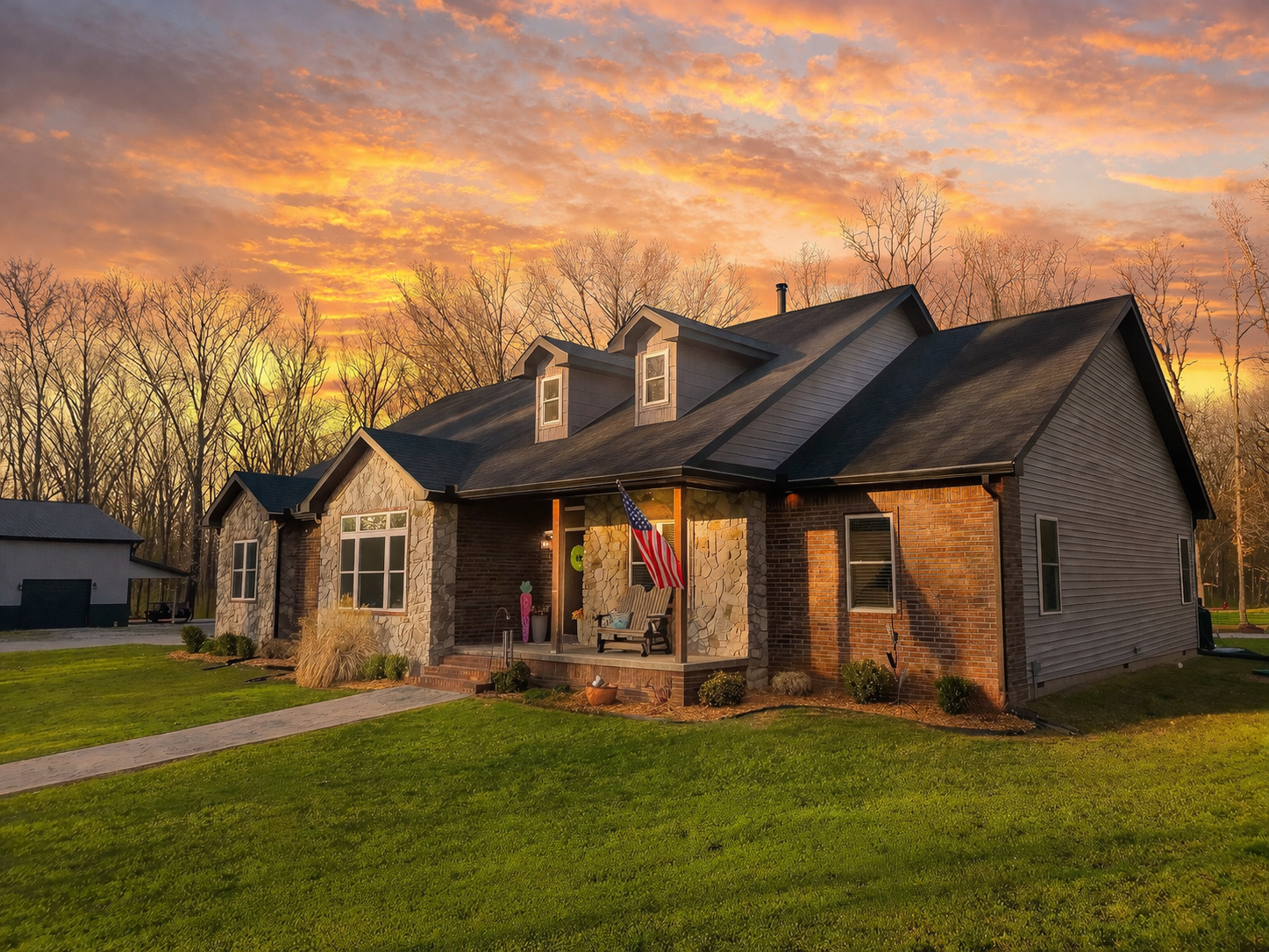 Brick ranch home with covered porch glowing under a vibrant orange and pink sunset sky, surrounded by lush green lawn.