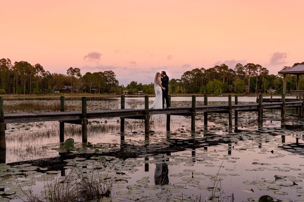 Couple sharing a romantic kiss on a wooden dock over a lily pad lake at sunset during their wedding.