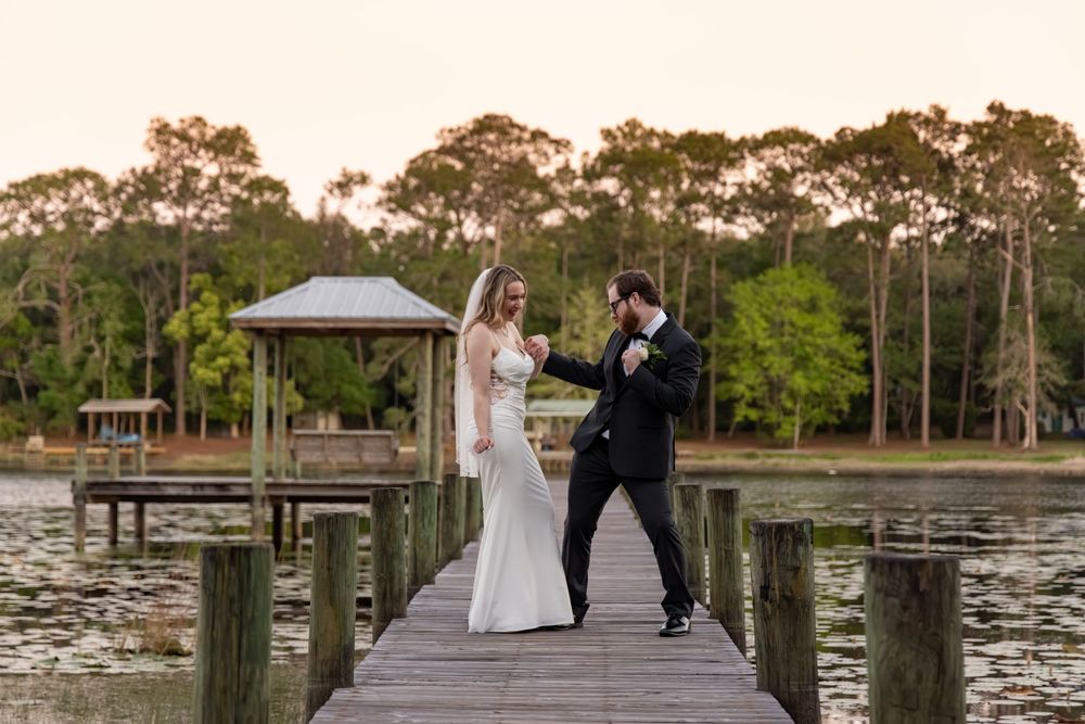 Bride and groom share a romantic moment on a wooden dock overlooking a serene lake at sunset.