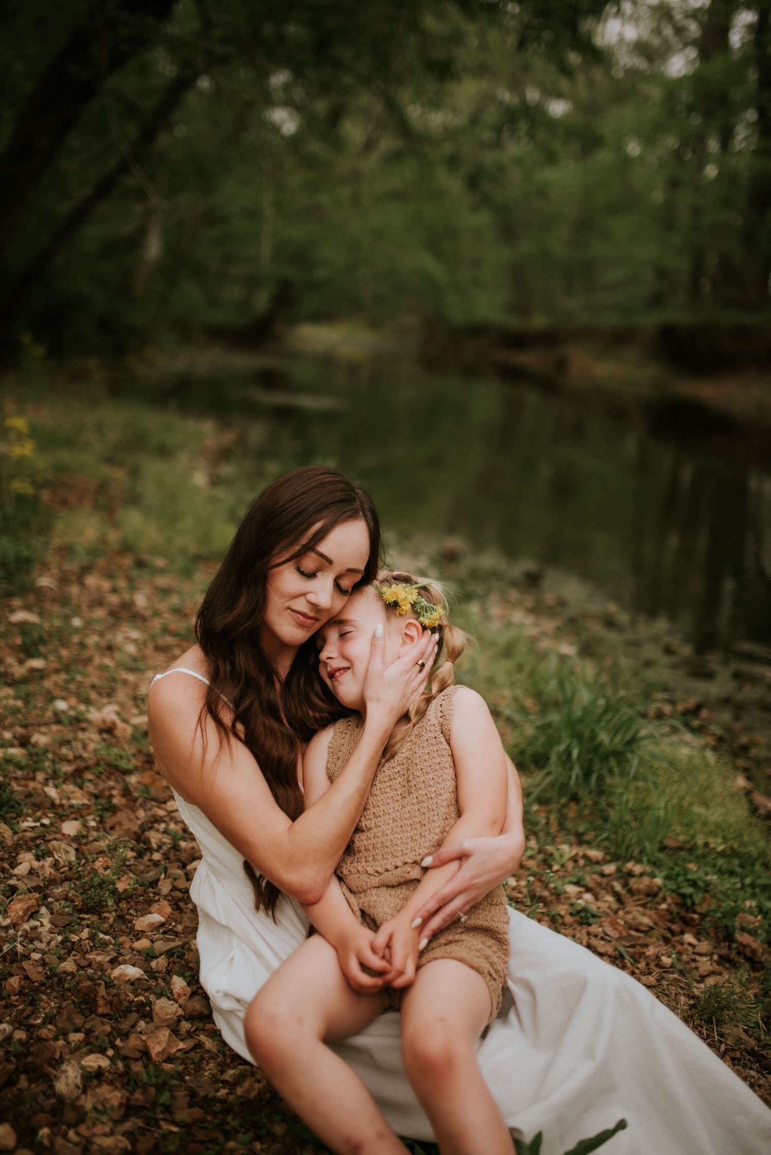 Mother strokes her daughters cheek while holding her in her lap at the creek in Clarksville, Tennessee.