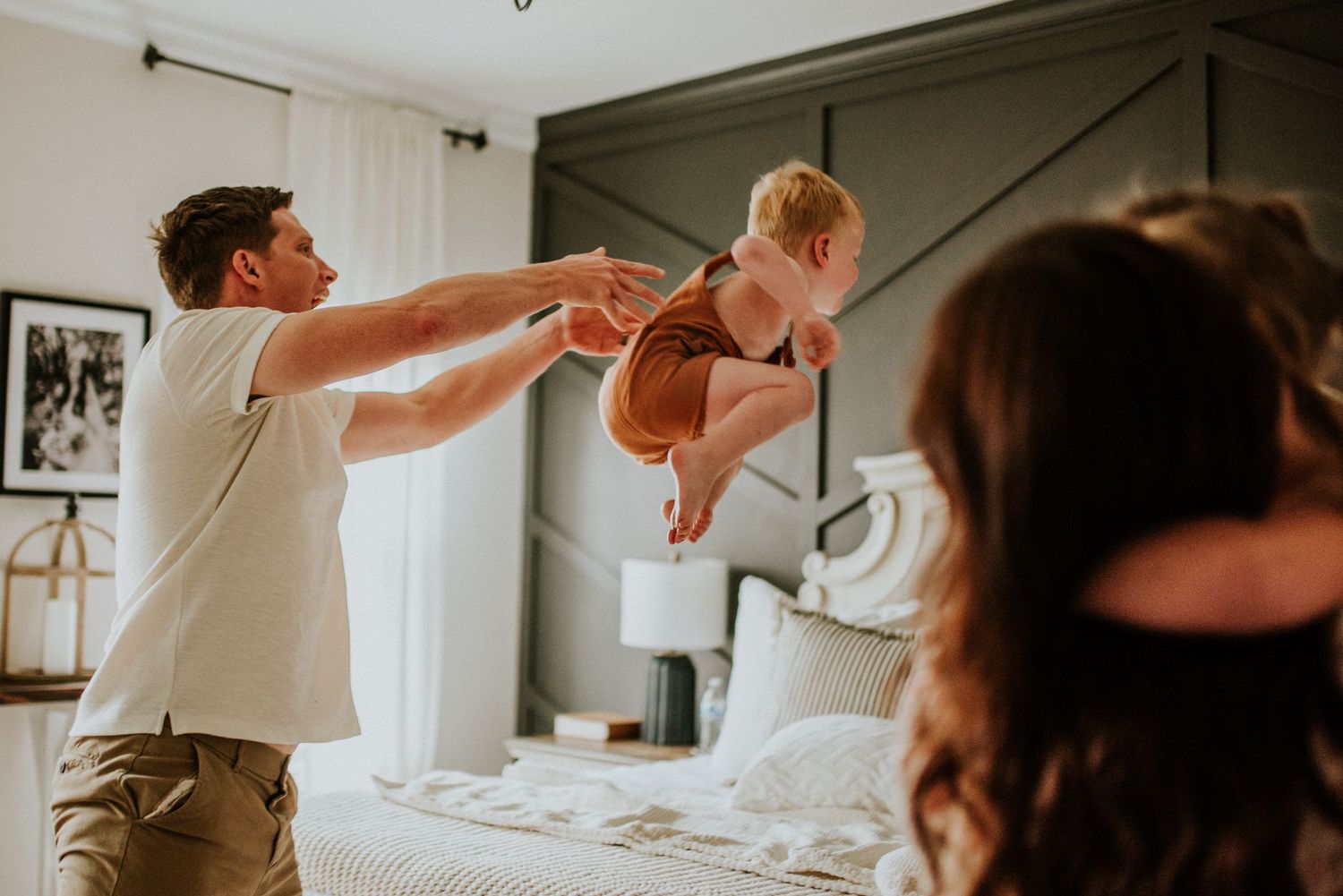 Father tosses son up on the bed in a joyful game during a lifestyle in home session with karina Cantu Photography.