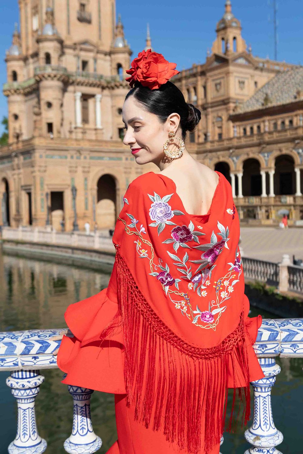 Woman in red flamenco dress with floral embroidery poses at Plaza de Espana, Seville, Spain.