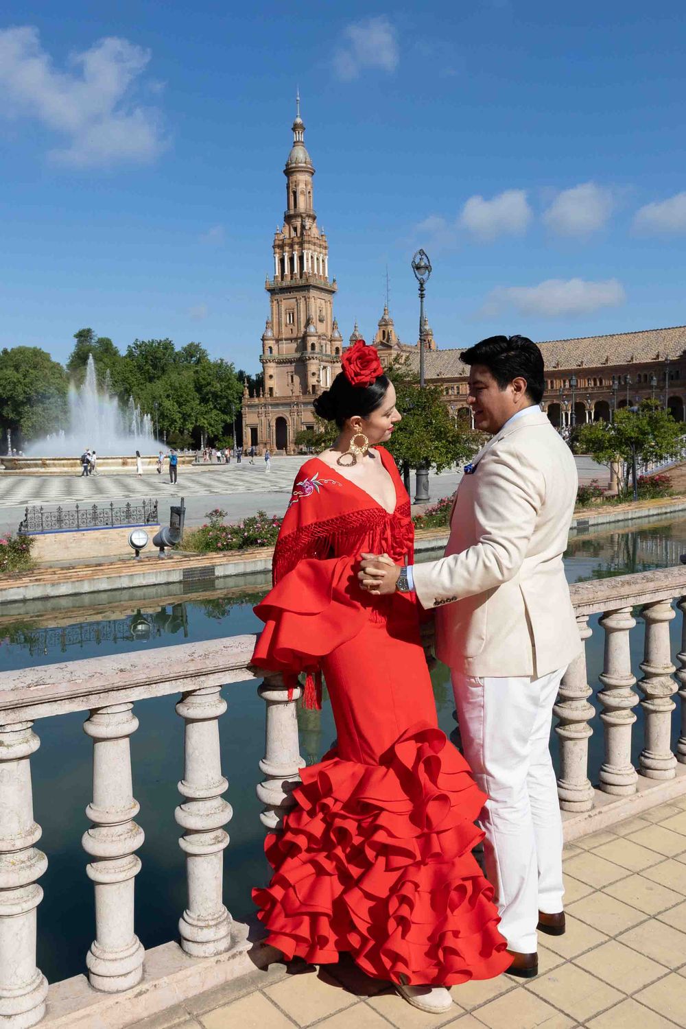Flamenco couple dancing at Plaza de España, Seville, woman in red ruffled dress, man in white suit, fountain backdrop.