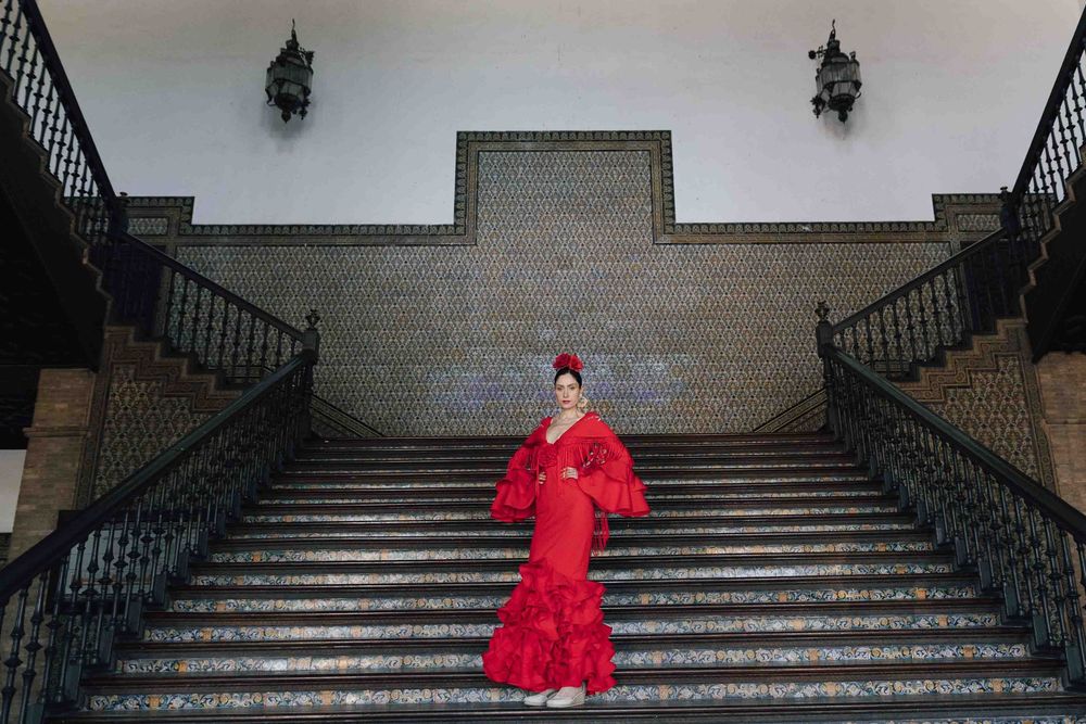Woman in red flamenco dress posing on ornate stone staircase with decorative tile wall backdrop.