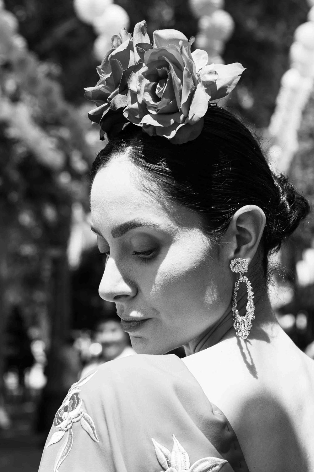 Black and white portrait of a woman with a rose hair accessory and elegant earrings at a Spanish festival.
