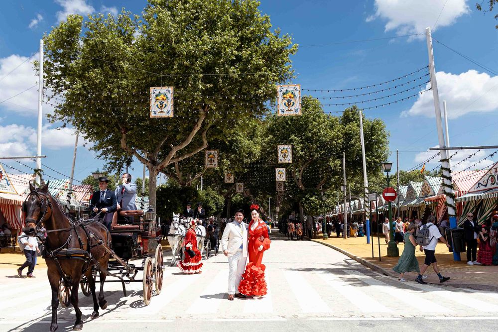 Traditional Spanish fair scene with horse-drawn carriage and women in flamenco dresses on a festive street.