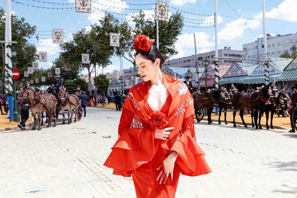 Woman in red flamenco dress with ruffles and flower hair accessory poses on a street during Seville's April Fair.