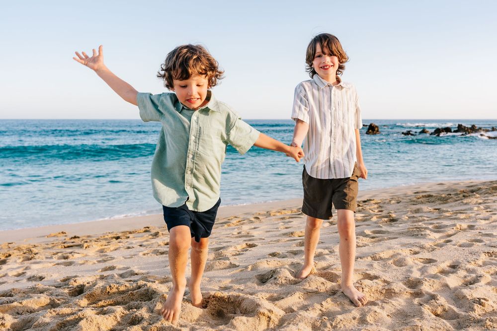 Two happy boys playing barefoot on a sunny sandy beach near the ocean on a clear day.