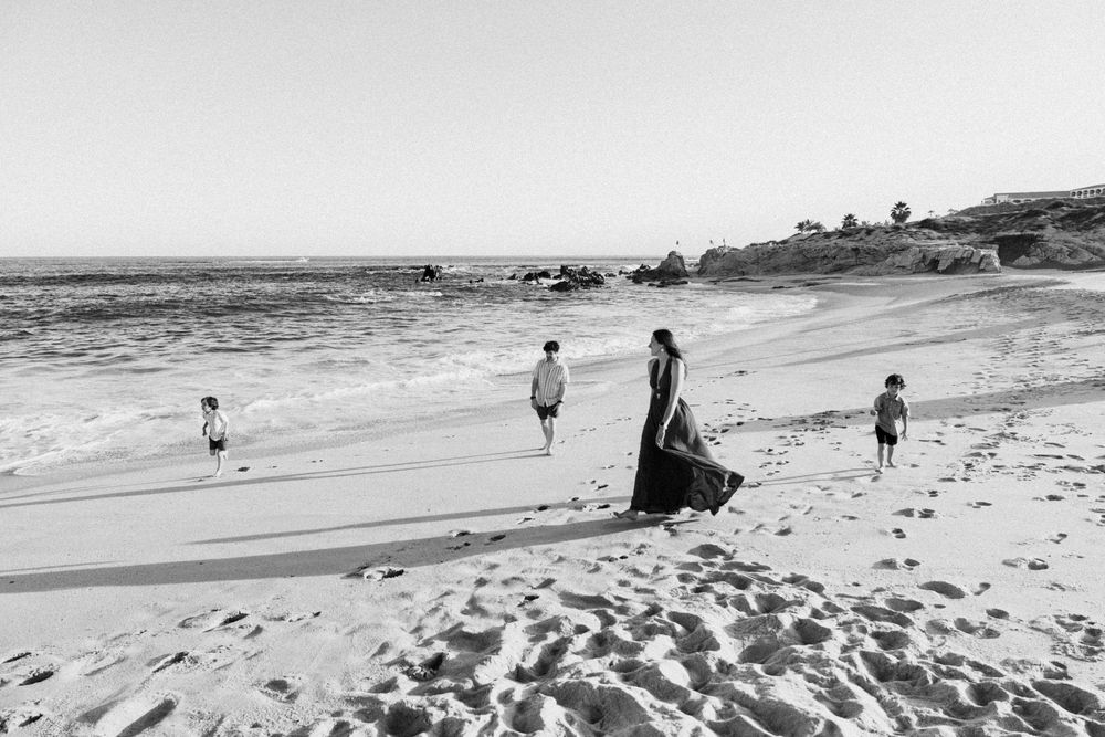 Black and white photo of a mother and three children walking along a wide sandy beach near the ocean.