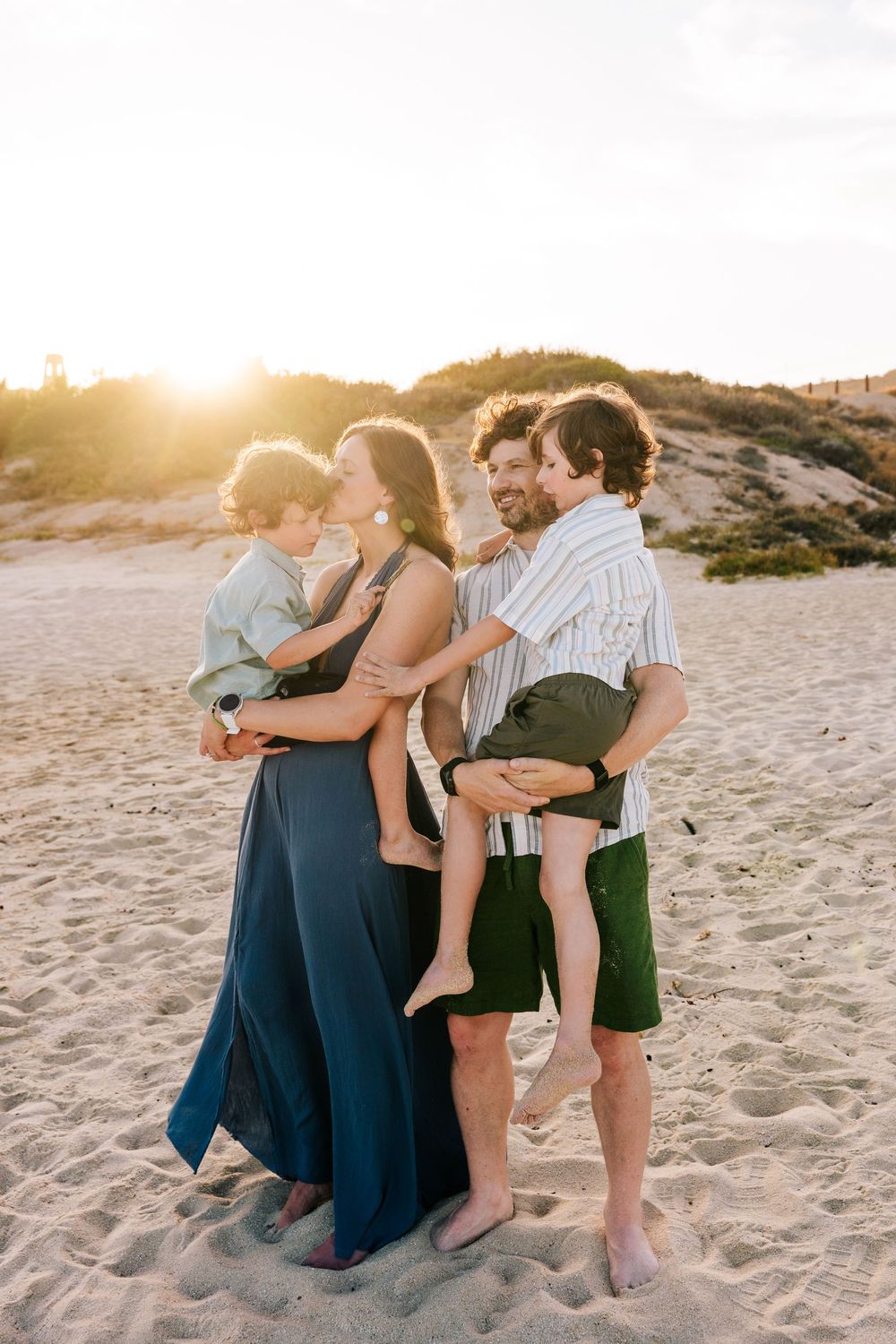 A happy family of four enjoys a golden sunset together on a sandy beach.