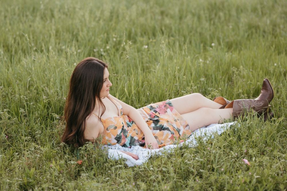 Woman in floral dress lying in green grass field with baby.