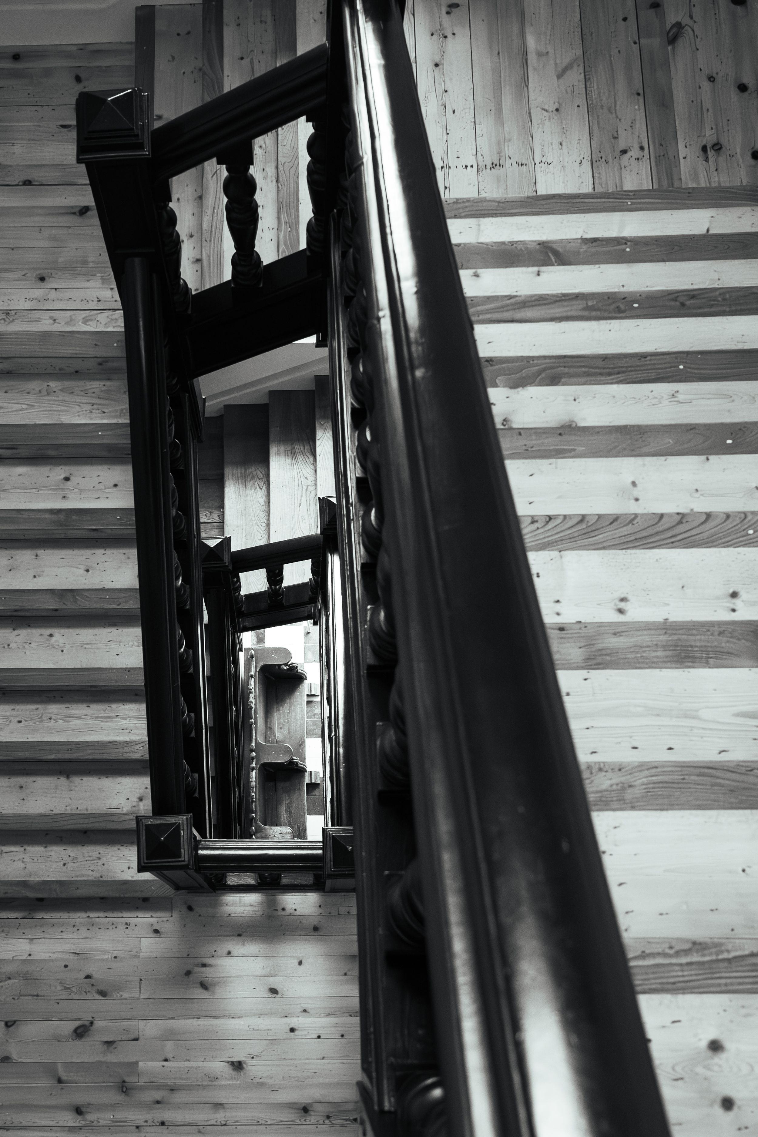 Black and white architectural photo of ornate wooden staircase railing and light pine steps from below.