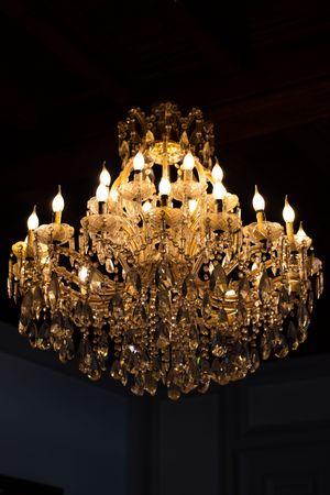 Ornate crystal chandelier with candle-style lights glowing warmly against a dark ceiling.