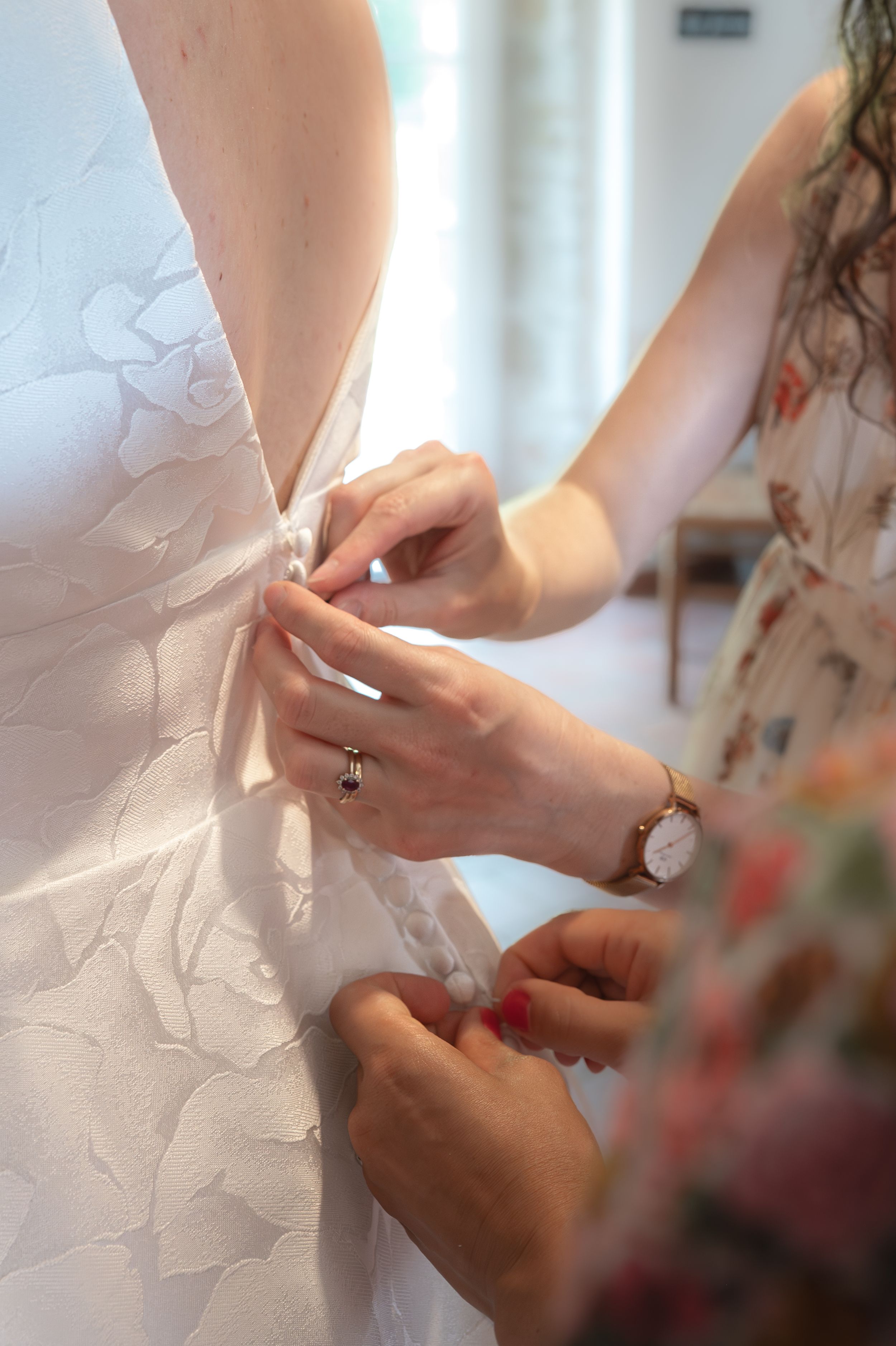 Des demoiselles d'honneur aident à boutonner le dos d'une robe de mariée blanche ; photographe premium stephanie lecaude