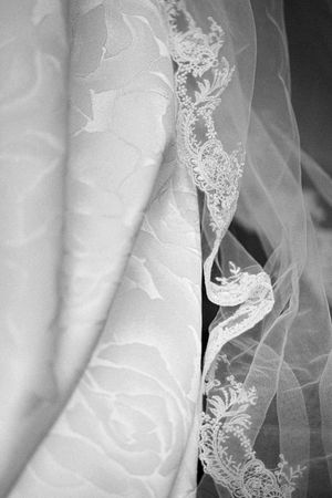 Black and white close-up of intricate lace trim on bridal veil and wedding gown.