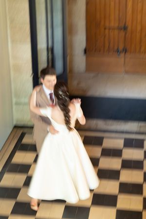 Blurred motion shot of bride and groom dancing on checkered tile floor near wooden door.