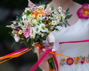 Une mariée tenant un bouquet de fleurs sauvages colorées orné de rubans roses et orange, vêtue d'une robe brodée. Photographe SL Stéphanie
