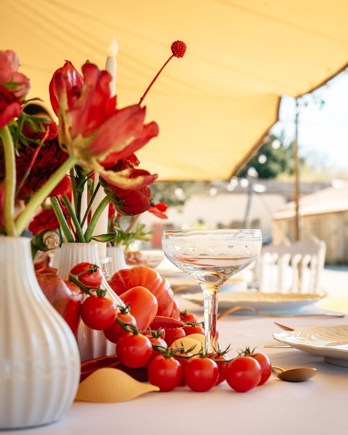 Elegant wedding table with red tulips, cherry tomatoes, and crystal coupe glass under a yellow tent.