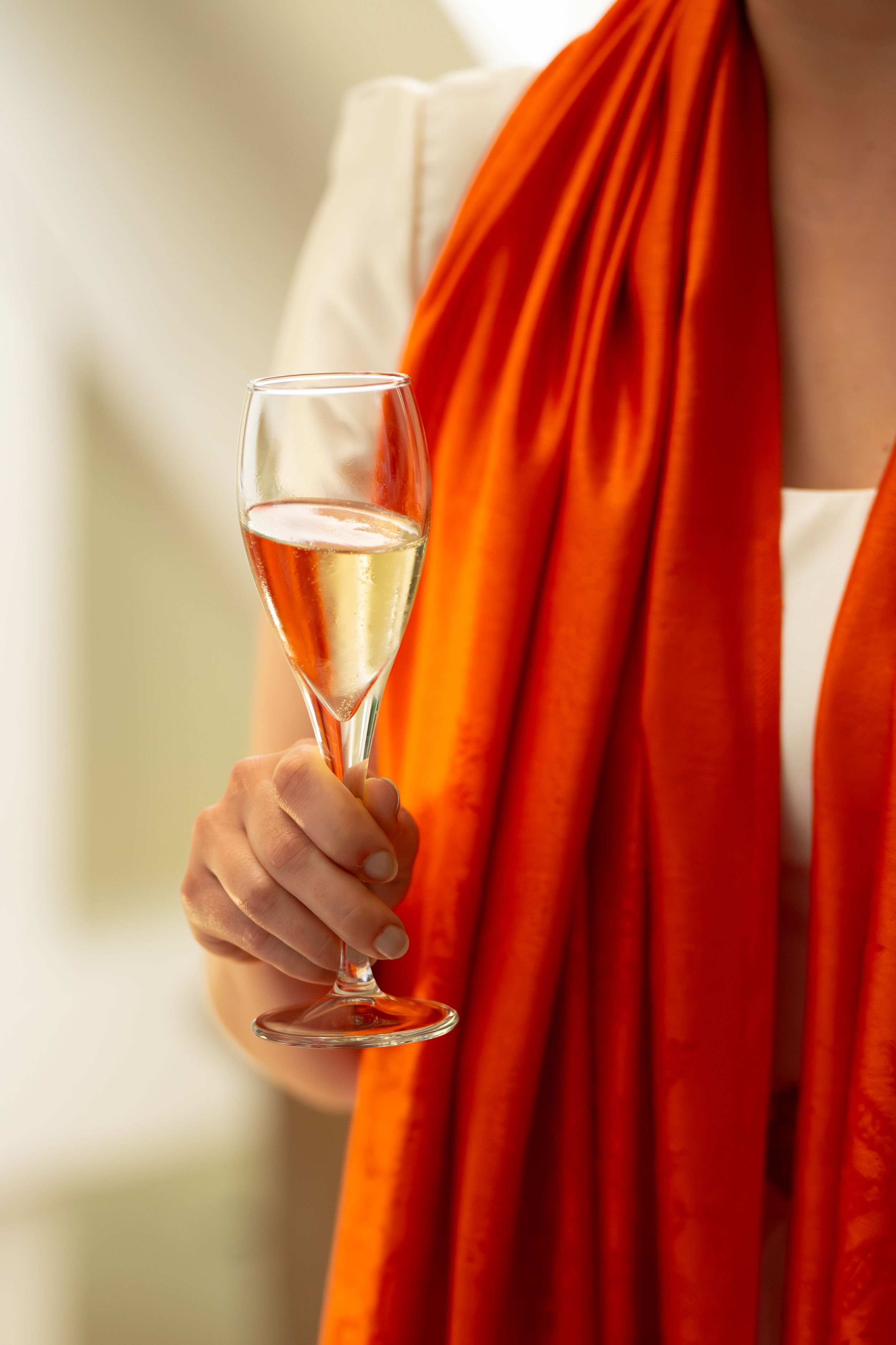 Woman in white outfit with bright orange scarf holding a champagne flute at a celebration.