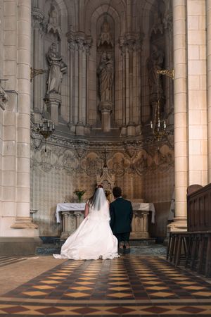 Les mariés, agenouillés ensemble en prière devant un autel richement décoré, à l'intérieur d'une cathédrale gothique en pierre.