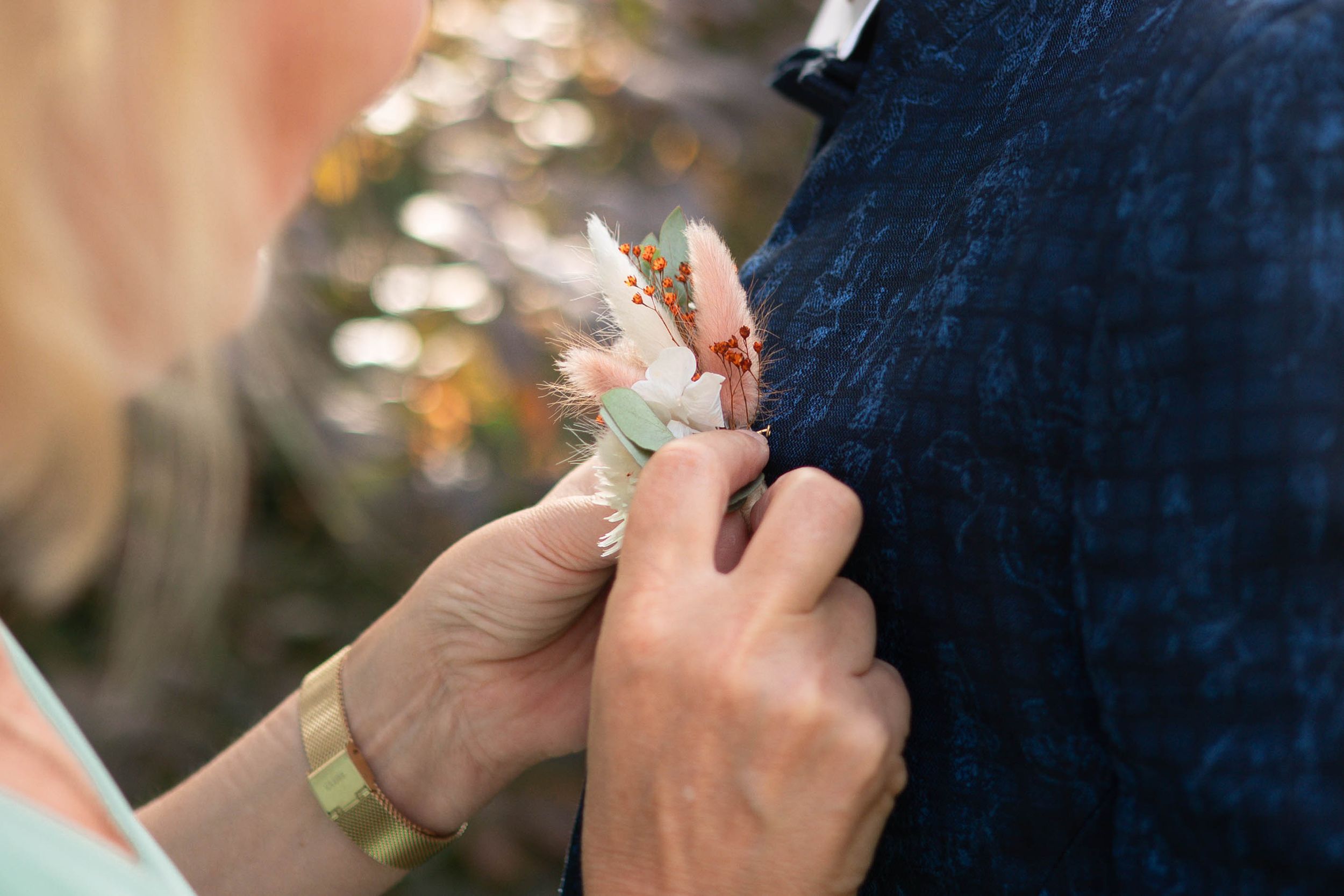 Close-up of hands pinning a floral boutonniere onto a navy blue suit jacket.
