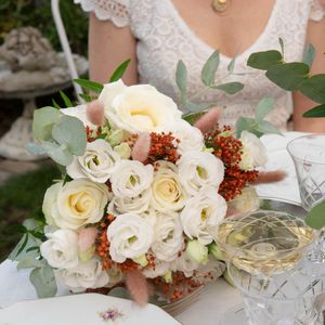 Une mariée tenant un bouquet de mariée composé de roses blanches, de baies orange et d'eucalyptus.
