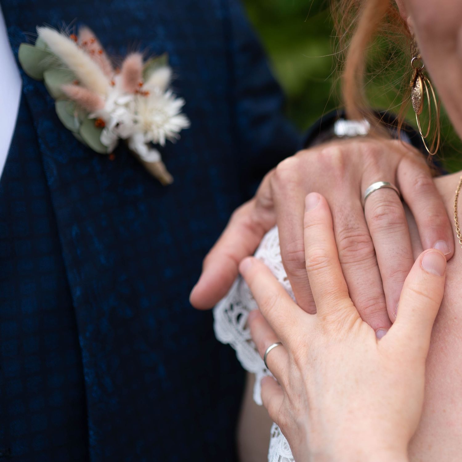 Photo des mains des mariés sur l'épaule de la mariée avec les alliances.