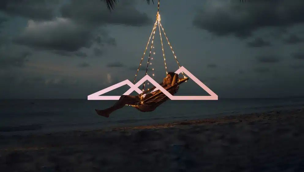 Person relaxing on a geometric neon swing installation on a beach at dusk with dramatic cloudy sky.
