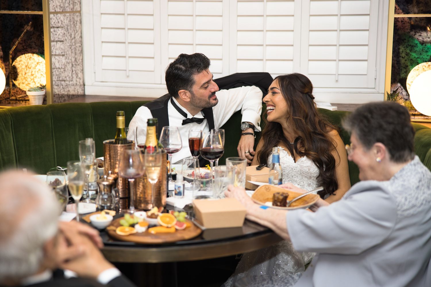 Bride and groom laughing together at wedding reception dinner table with wine and elegant decor.