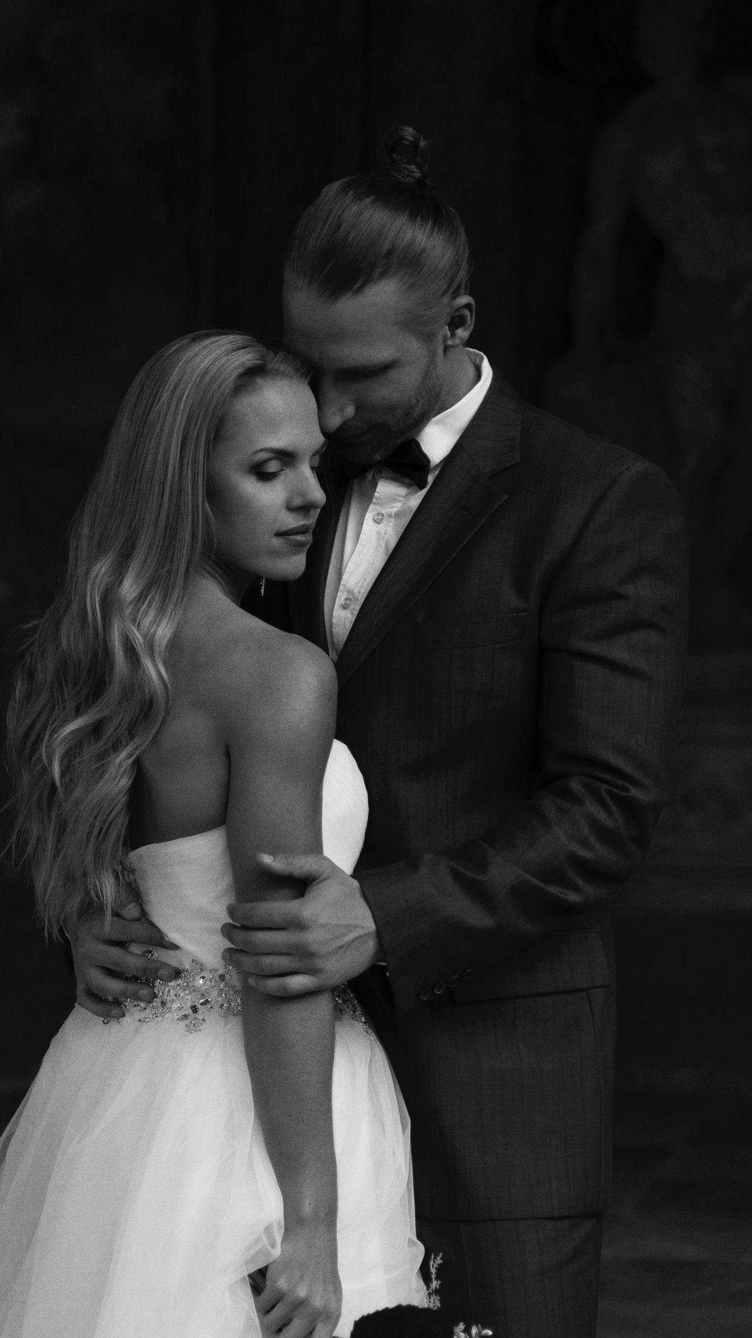 Black and white wedding photo of bride in strapless gown and groom in suit with bow tie embracing romantically.