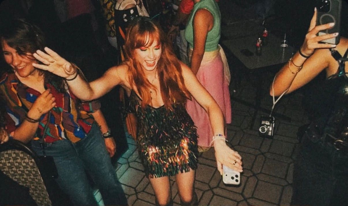 Woman in sequined mini dress dancing at a party while others take photos on smartphones.