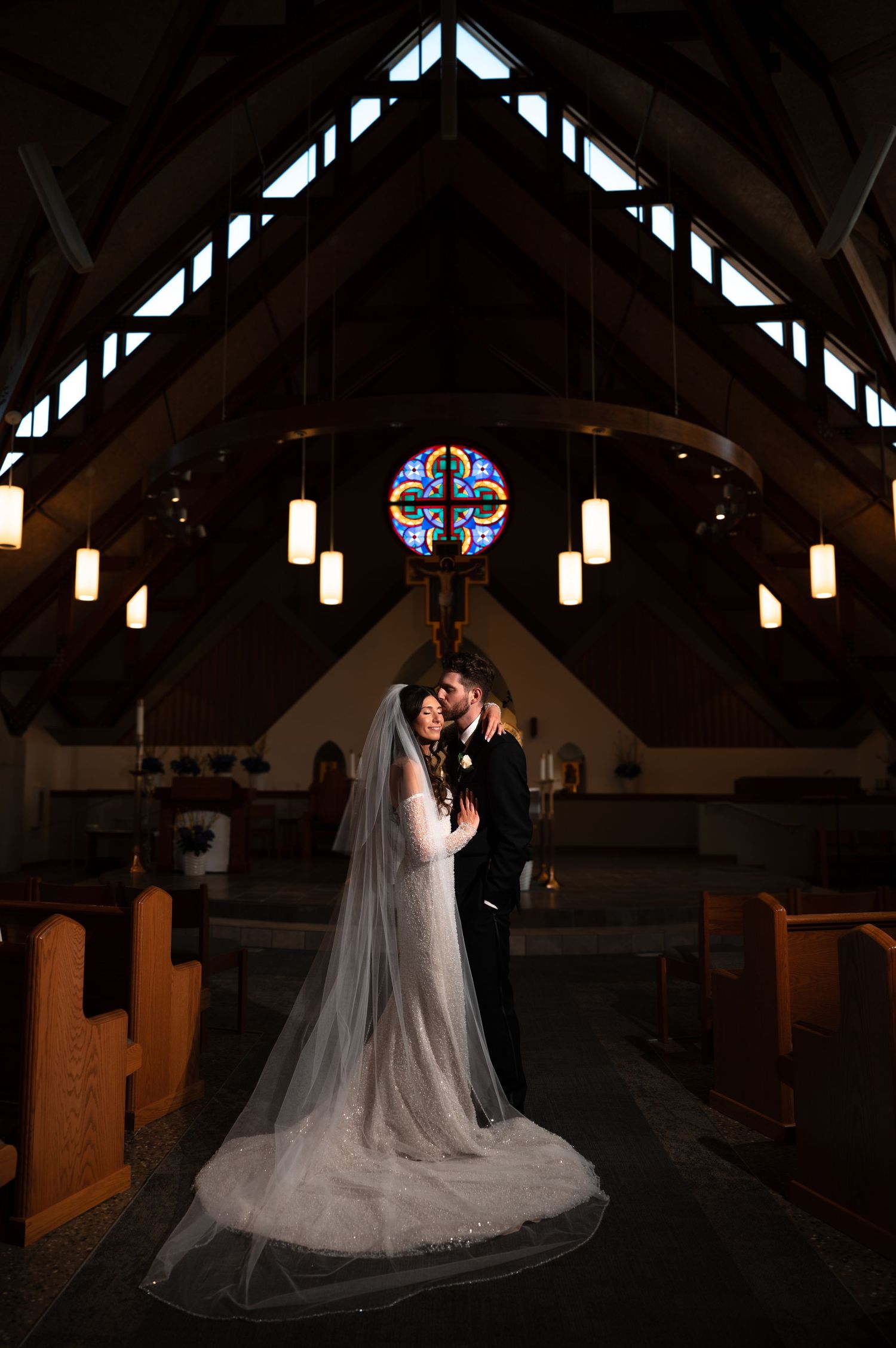 Bride and groom share an intimate moment, smiling at each other, bride in off-shoulder gown, groom in dark suit.