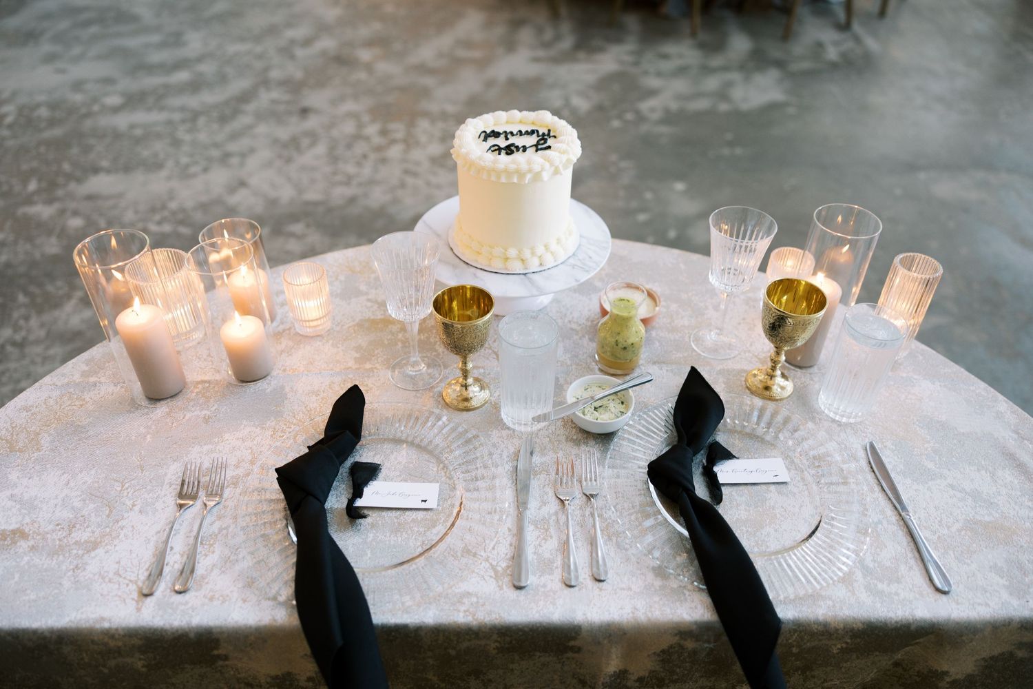 Elegant wedding table setting with gold goblets, black napkins, crystal plates, and marble centerpiece on a stone table.