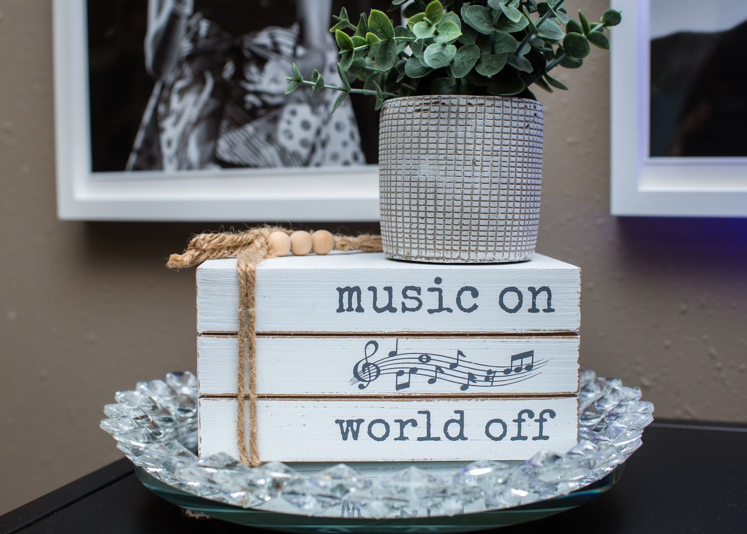 Decorative stacked books with music notes reading 'Music On World Off' on a crystal tray with a plant.