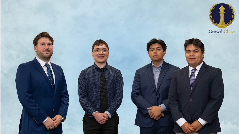 Four professional men in suits and dress shirts pose together against a light blue background for a corporate team photo.